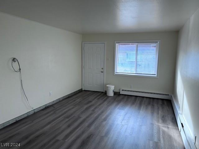 unfurnished room featuring baseboard heating and dark wood-type flooring