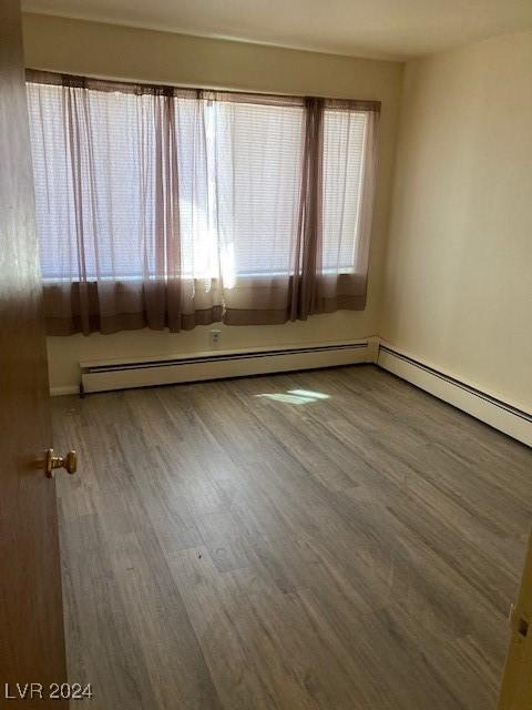 unfurnished room with hardwood / wood-style floors and a baseboard heating unit