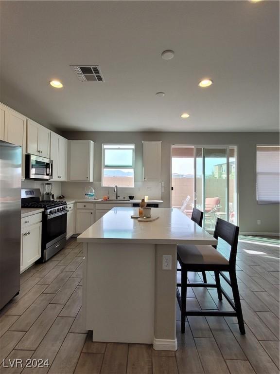 kitchen with white cabinetry, a kitchen island, light wood-type flooring, and appliances with stainless steel finishes