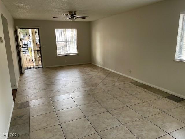 tiled empty room featuring a textured ceiling, a wealth of natural light, and ceiling fan