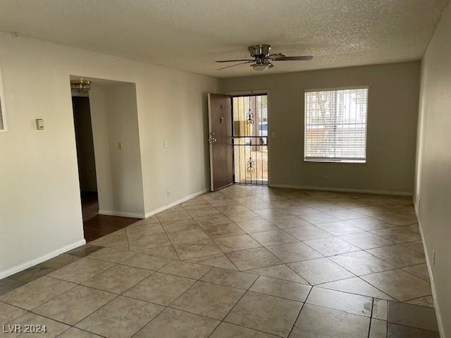 empty room with ceiling fan, light tile patterned floors, and a textured ceiling