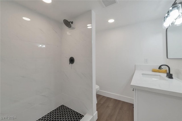 bathroom with a tile shower, wood-type flooring, toilet, and vanity