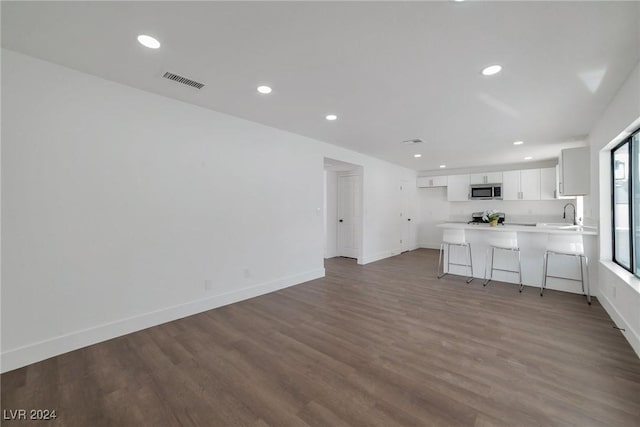 kitchen with white cabinetry, kitchen peninsula, a breakfast bar area, and dark hardwood / wood-style flooring