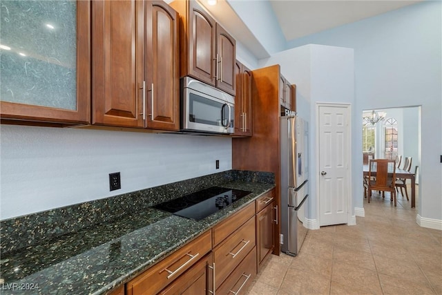 kitchen with light tile patterned floors, appliances with stainless steel finishes, a notable chandelier, and dark stone counters