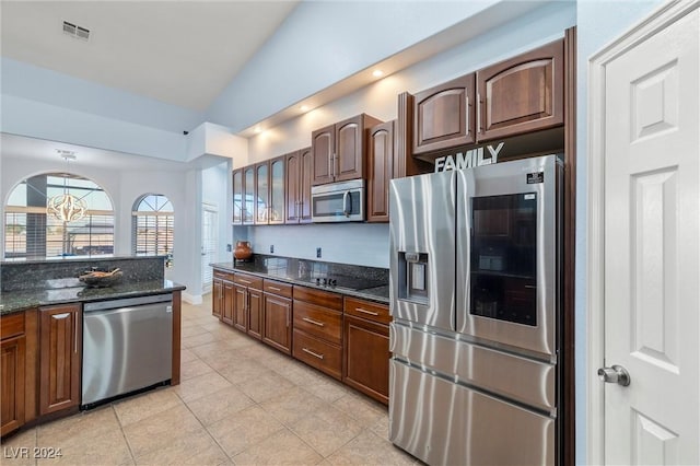 kitchen featuring vaulted ceiling, light tile patterned floors, appliances with stainless steel finishes, and dark stone countertops