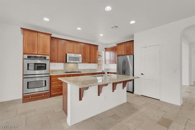 kitchen with light stone counters, stainless steel appliances, sink, a breakfast bar area, and an island with sink