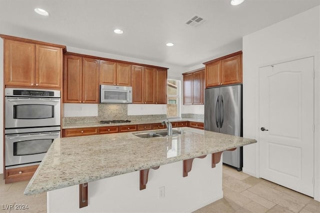 kitchen with sink, light stone counters, a kitchen bar, a center island with sink, and appliances with stainless steel finishes