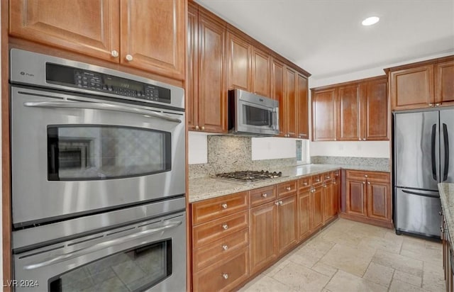 kitchen featuring decorative backsplash, appliances with stainless steel finishes, and light stone counters