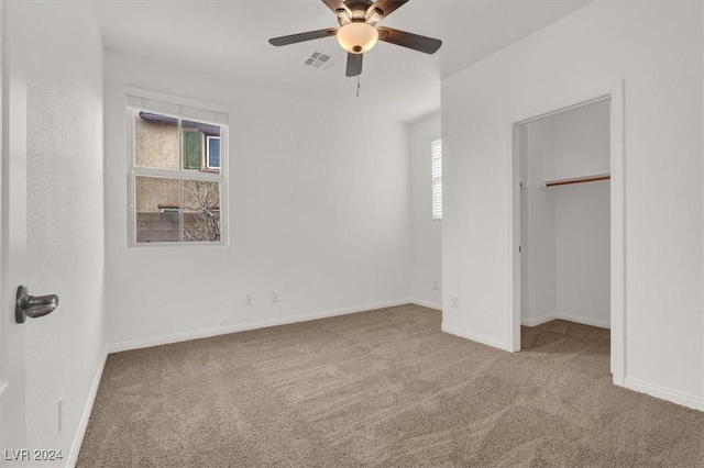 unfurnished bedroom with a closet, light colored carpet, a spacious closet, and ceiling fan