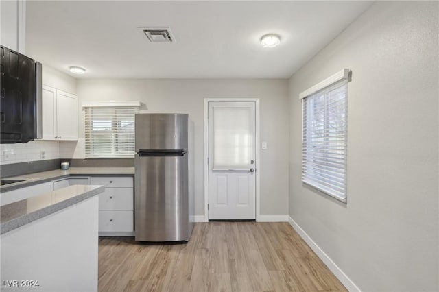 kitchen with white cabinets, stainless steel fridge, decorative backsplash, and light hardwood / wood-style flooring