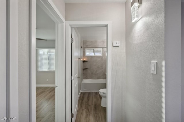 bathroom with plenty of natural light, wood-type flooring, tiled shower / bath combo, and toilet