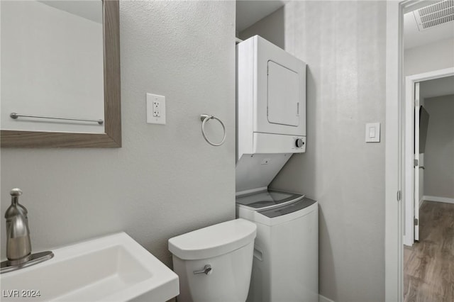 bathroom with hardwood / wood-style floors, toilet, sink, and stacked washer and clothes dryer