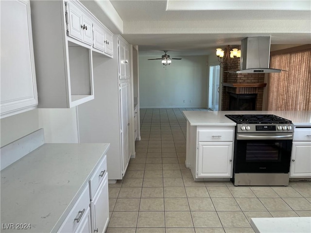 kitchen featuring light tile patterned floors, light countertops, white cabinets, stainless steel gas range, and wall chimney exhaust hood