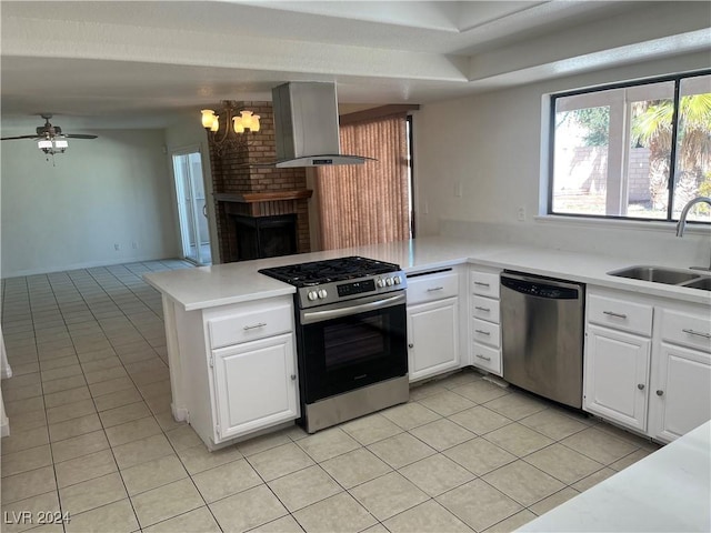 kitchen featuring light tile patterned floors, stainless steel appliances, a sink, a peninsula, and wall chimney exhaust hood