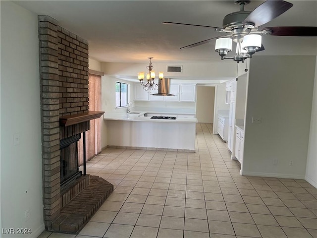 kitchen with light tile patterned floors, white cabinets, wall chimney exhaust hood, a peninsula, and a fireplace