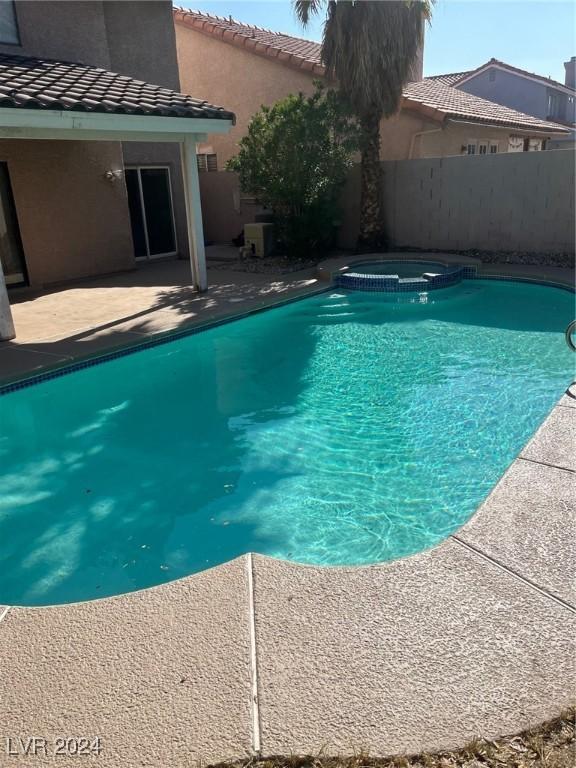 view of pool with a pool with connected hot tub, fence, and a patio