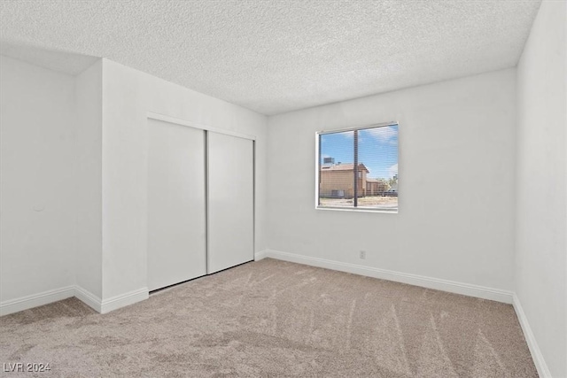 unfurnished bedroom featuring a textured ceiling, light colored carpet, and a closet