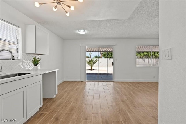 kitchen with decorative backsplash, white cabinetry, sink, and light hardwood / wood-style flooring