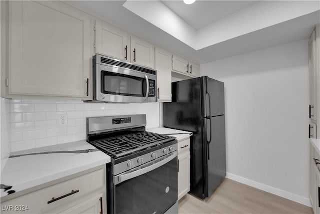 kitchen with light stone countertops, white cabinetry, stainless steel appliances, light hardwood / wood-style flooring, and decorative backsplash