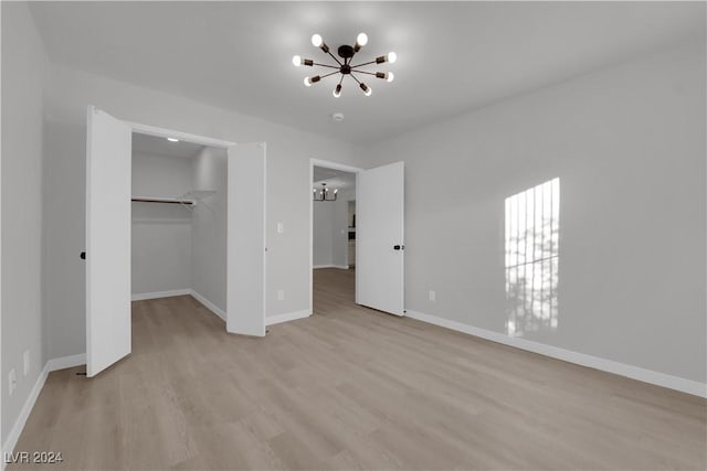 unfurnished bedroom with a closet, a walk in closet, light hardwood / wood-style flooring, and an inviting chandelier