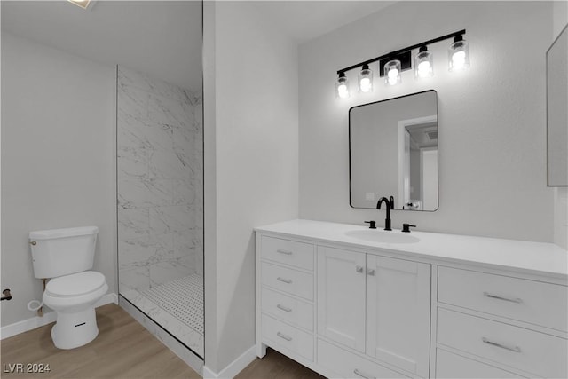 bathroom featuring toilet, hardwood / wood-style floors, vanity, and tiled shower