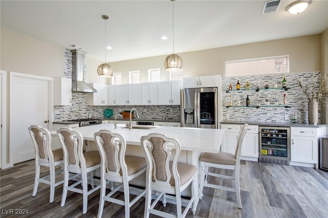 kitchen featuring hanging light fixtures, an island with sink, stainless steel fridge with ice dispenser, beverage cooler, and wall chimney exhaust hood