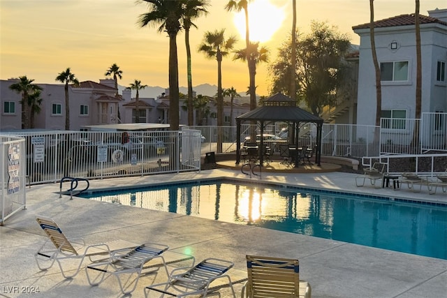 pool at dusk with a gazebo and a patio area