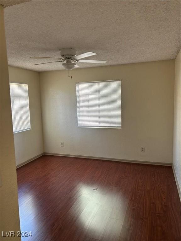 empty room with a textured ceiling, dark hardwood / wood-style flooring, a wealth of natural light, and ceiling fan