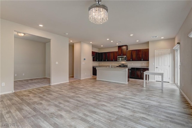 kitchen with appliances with stainless steel finishes, light hardwood / wood-style floors, a kitchen island with sink, and a notable chandelier