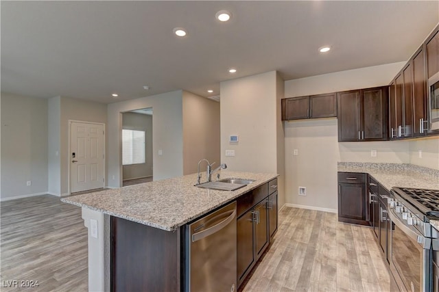 kitchen featuring light wood-type flooring, light stone counters, stainless steel appliances, sink, and a center island with sink