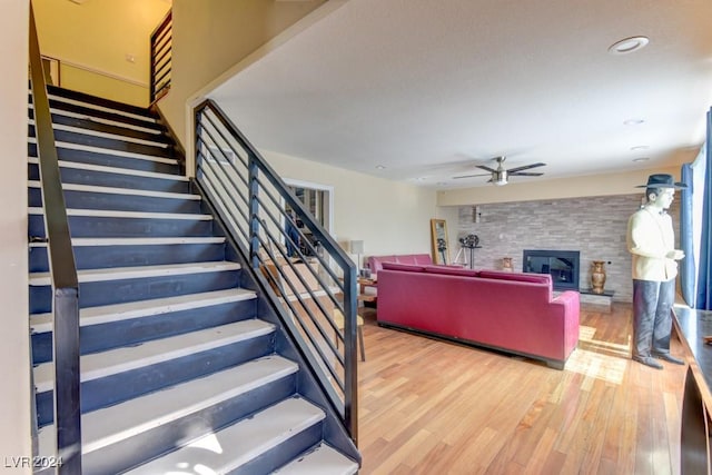 stairs featuring ceiling fan, a stone fireplace, and hardwood / wood-style floors