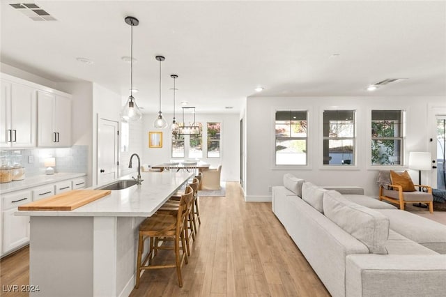 kitchen featuring a kitchen island with sink, white cabinets, light hardwood / wood-style flooring, tasteful backsplash, and a breakfast bar area