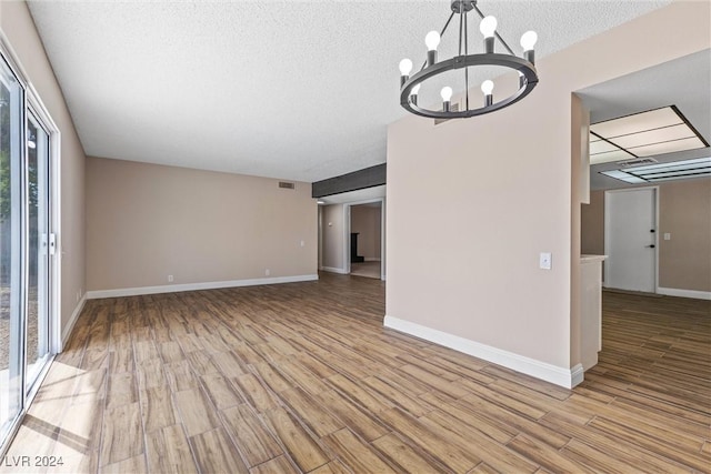 unfurnished living room with a chandelier, a textured ceiling, and light wood-type flooring