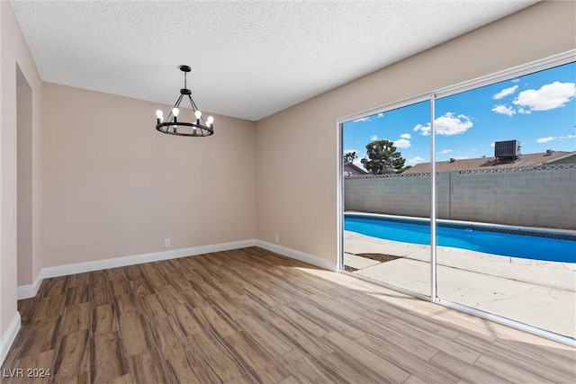 empty room featuring hardwood / wood-style flooring, a textured ceiling, and a chandelier