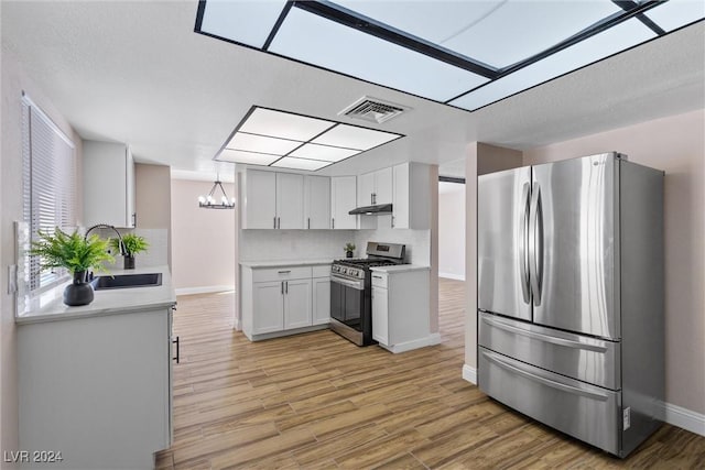 kitchen featuring white cabinets, sink, light wood-type flooring, appliances with stainless steel finishes, and decorative light fixtures