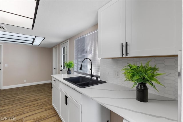 kitchen with light stone countertops, light wood-type flooring, tasteful backsplash, sink, and white cabinetry