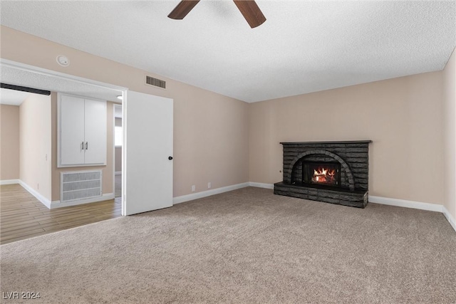 unfurnished living room featuring light carpet, a textured ceiling, a brick fireplace, and ceiling fan