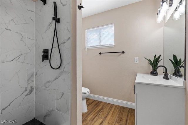 bathroom with hardwood / wood-style flooring, vanity, toilet, and a tile shower