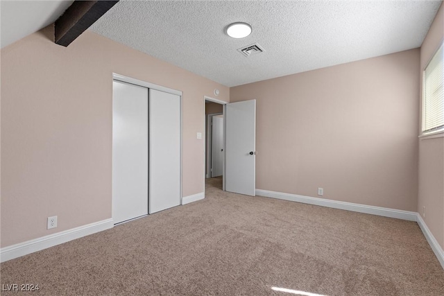 unfurnished bedroom featuring a textured ceiling, lofted ceiling with beams, light colored carpet, and a closet