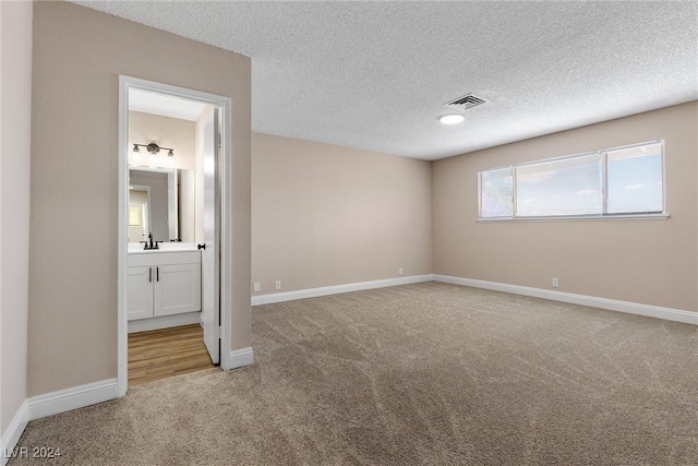 unfurnished bedroom with sink, carpet floors, a textured ceiling, and connected bathroom