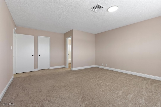 unfurnished bedroom with ensuite bath, light colored carpet, and a textured ceiling