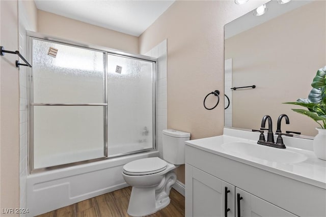 full bathroom featuring hardwood / wood-style floors, vanity, toilet, and bath / shower combo with glass door