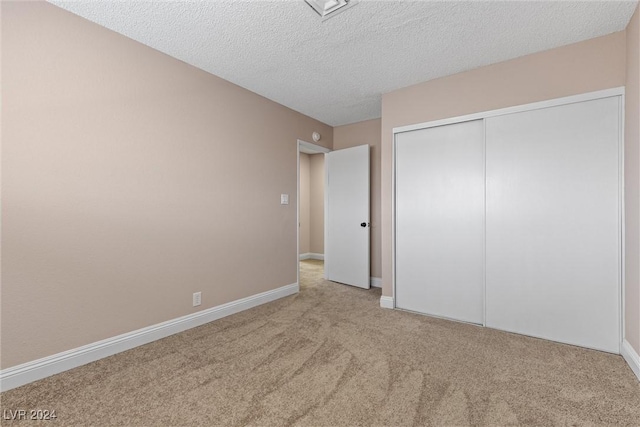 unfurnished bedroom featuring a textured ceiling, light carpet, and a closet