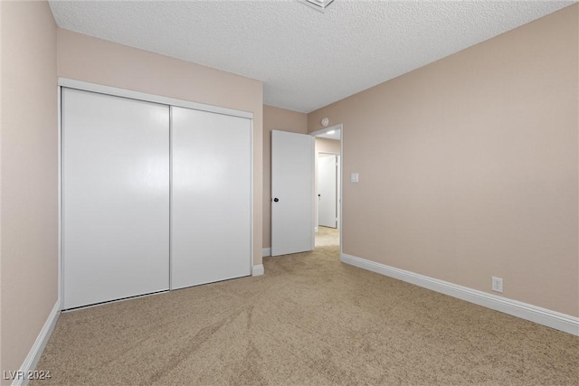 unfurnished bedroom with light colored carpet, a textured ceiling, and a closet