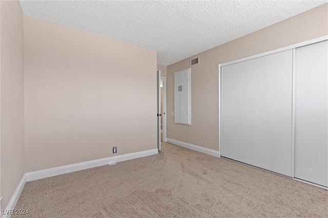 unfurnished bedroom with a closet, light colored carpet, and a textured ceiling