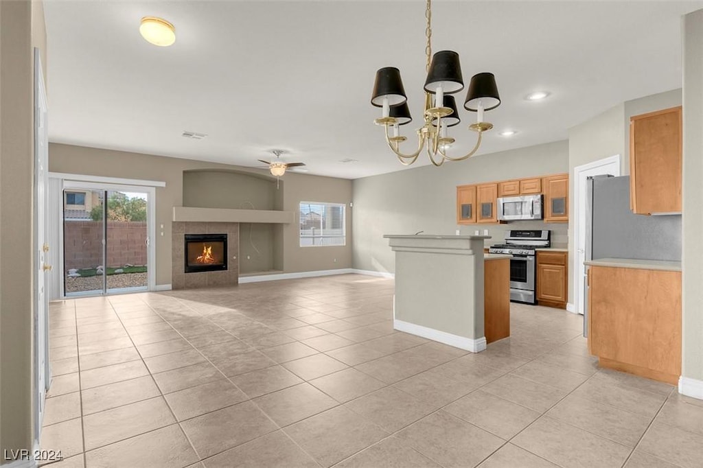 kitchen with hanging light fixtures, appliances with stainless steel finishes, a tile fireplace, a healthy amount of sunlight, and ceiling fan with notable chandelier