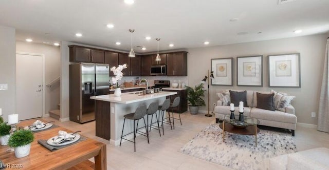 kitchen with appliances with stainless steel finishes, dark brown cabinetry, a center island with sink, and a kitchen breakfast bar