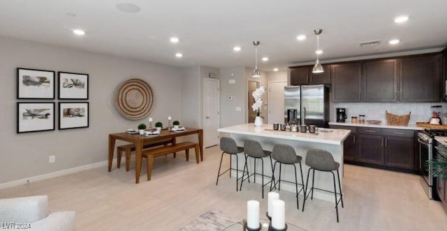 kitchen with hanging light fixtures, stainless steel appliances, backsplash, an island with sink, and a kitchen bar