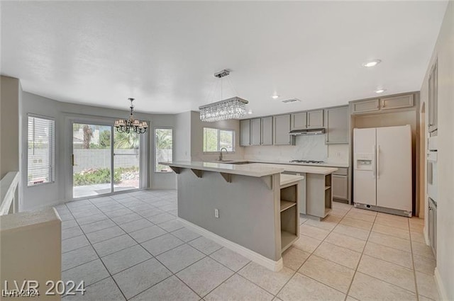 kitchen with a center island, an inviting chandelier, a kitchen breakfast bar, hanging light fixtures, and white fridge with ice dispenser