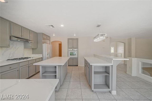 kitchen featuring gray cabinetry, a kitchen island, pendant lighting, white appliances, and light tile patterned floors